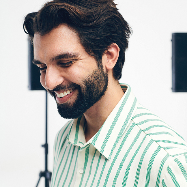 cantor Silva sorrindo com os olhos fechados. Ele veste uma camisa listrada Hering
